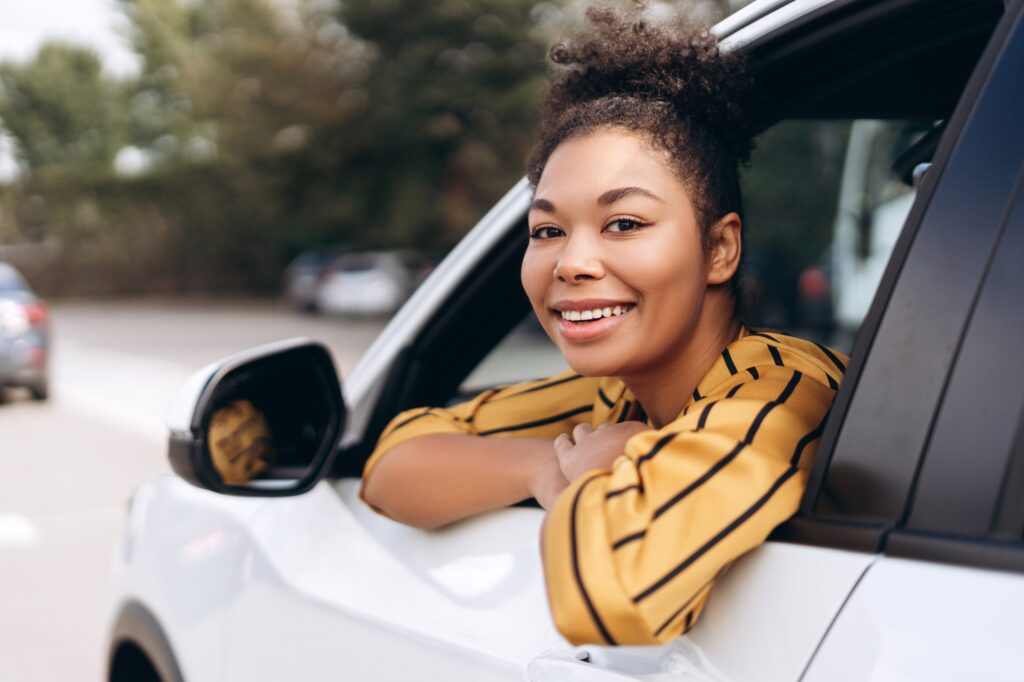 Smiling pretty African woman sitting at her car while looking at open window
